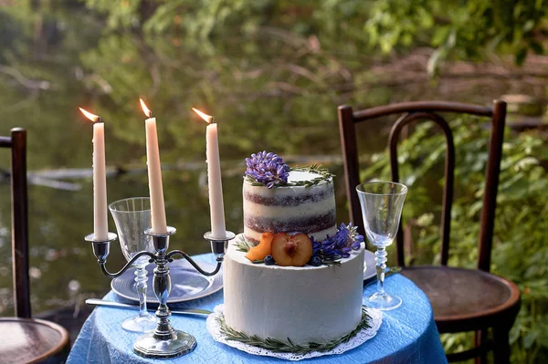 Romantic wedding dinner, in the Park by the water. Lots of green. Table for a romantic wedding dinner, date. The Park by the lake. In a blue color. With white bunk cake and serving for 2 persons.