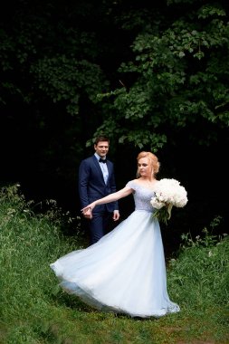 Gelin, güzel bir mavi elbise içinde dönüyor. Damat bir mesafede duran ve hayran. Park veya orman. Düğün yürüyüş ve fotoğraf ateş