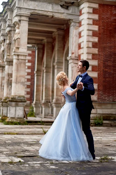 The bride and groom dancing around the columns of the old estate. A tall groom, and a bride with blond hair. Blue wedding dress.Wedding walk and photo shoot