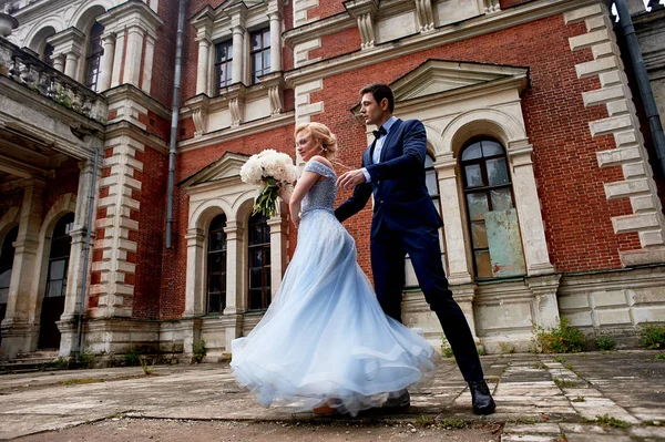 The bride and groom dancing around the columns of the old estate. A tall groom, and a bride with blond hair. Blue wedding dress.Wedding walk and photo shoot