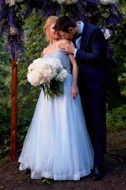 Kemer, Gelin ve damat standında beyaz peonies büyük bir buket çiçek ile dekore edilmiştir. Yerinde kaydı Park Düğün yürüyüş ve fotoğraf ateş