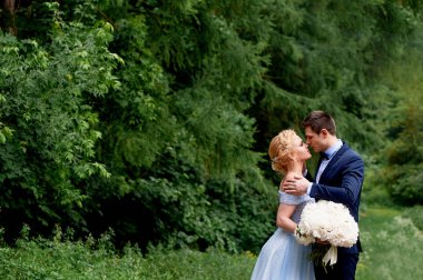 Düğün fotoğraf çekimi ve yürüyüş. Damat ve gelin, gelinler mavi elbise ve peonies bir buket. Park, yeşil ağaçlar, alanlar, çalılar arka plan üzerinde.