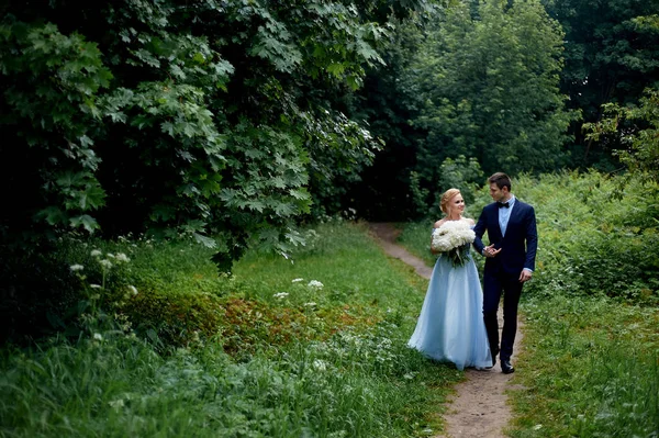 Düğün fotoğraf çekimi ve yürüyüş. Damat ve gelin, gelinler mavi elbise ve peonies bir buket. Park, yeşil ağaçlar, alanlar, çalılar arka plan üzerinde. — Stok fotoğraf