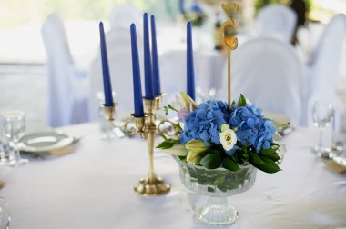 Tablo klasik bir tasarıma sahip. Vazoda bir yüksek ortancaları ve lilyum, Altın şamdan mavi mum ile bir kompozisyon ile. Dekor ve floristik