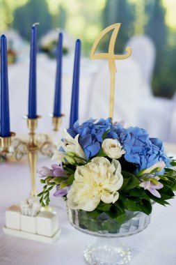 Tablo klasik bir tasarıma sahip. Vazoda bir yüksek ortancaları ve lilyum, Altın şamdan mavi mum ile bir kompozisyon ile. Dekor ve floristik