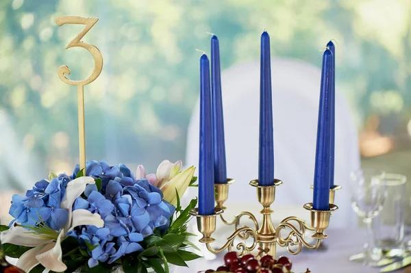 表与经典设计。在一个高花瓶与绣球和百合的组合, 一个金色烛台与蓝色蜡烛。装饰和植物 — 图库照片