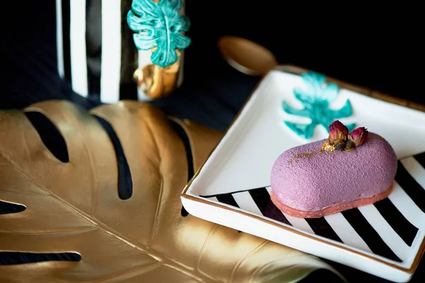 Pastel de mousse de fruta púrpura, sobre un hermoso platillo. Sobre un fondo oscuro, con una lámina de monstera pintada en pintura dorada. Arte culinario — Foto de Stock