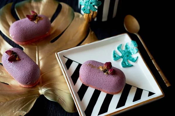 Purple fruit mousse cake, on a beautiful saucer.On a dark background, with a sheet of monstera painted in gold paint. Culinary art