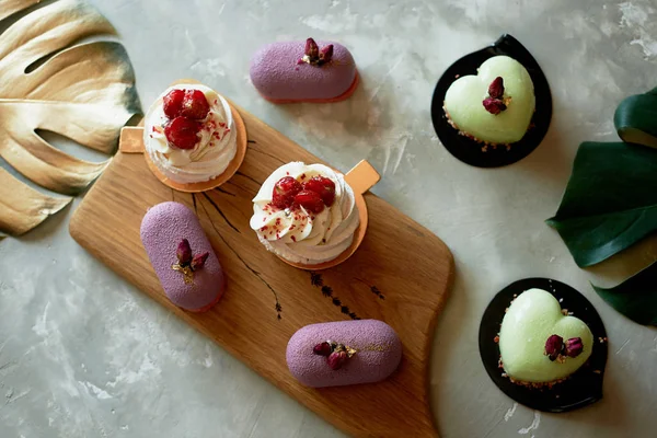 Purple fruit mousse cake, meringue Anna Pavlova on a wooden Board.Pistachio mousse cake. Culinary art