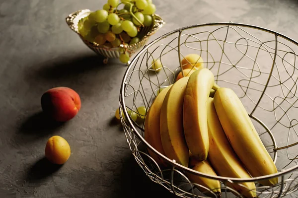 Свежие и сочные фрукты, бананы, персики, виноград на сером фоне. — стоковое фото
