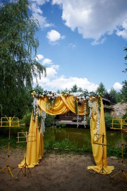 Arch Sarı kumaş ve çiçeklerle süslenmiş açık havada düğün töreni için.