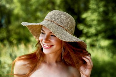 A sophisticated red-haired girl in a simple linen dress, in a light wide-brimmed hat.Model look. Natural beauty. Artistic portrait. Wide happy smile clipart
