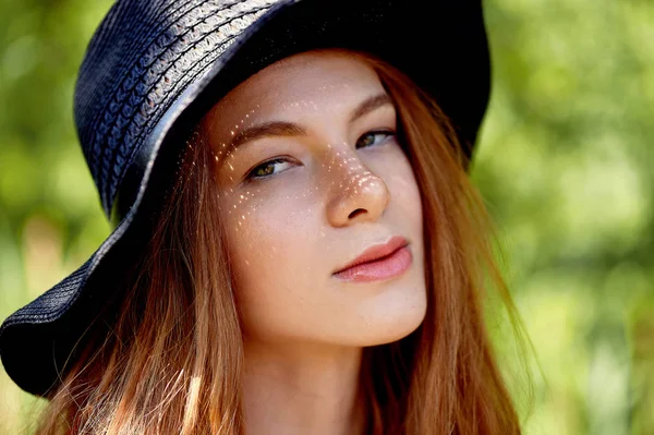 Портрет рудоволоса дівчина з довгим волоссям, в чорному широковольтному капелюсі. Сонце робить веснянки на щоках. Сонячні плями на обличчі — стокове фото
