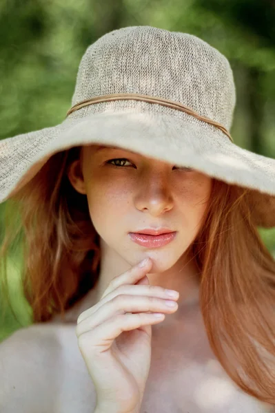 A sophisticated red-haired girl in a simple linen dress, in a light wide-brimmed hat.Model look. Natural beauty. Artistic portrait