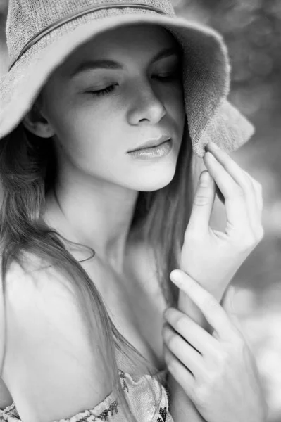 A sophisticated red-haired girl in a simple linen dress, in a light wide-brimmed hat.Model look. Natural beauty. Artistic portrait. Keeps the brim. Black and white