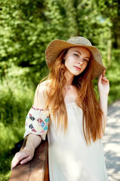 A sophisticated red-haired girl in a simple linen dress, in a light wide-brimmed hat.Model look. Natural beauty. Artistic portrait