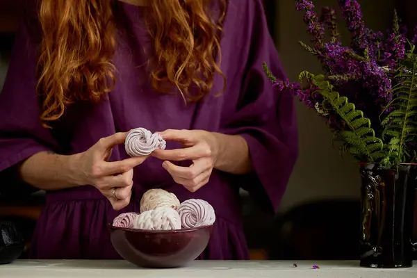 Fille aux cheveux roux dans une robe violette rompt un morceau de guimauve. Ensuite, un bol de dessert et un vase — Photo