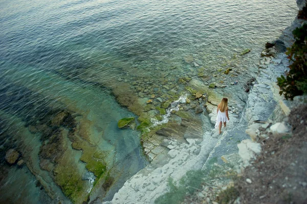 Mała postać dziewczyny na tle morza, skały, urwiska. Człowiek i elementy. Reszty morza. Biała tunika macha. — Zdjęcie stockowe