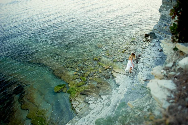 Bir kızın deniz, kayalar, cliff arka plan üzerinde küçük bir rakam. Adam ve öğeleri. Deniz dinlenme. Tunik sallayarak beyaz. — Stok fotoğraf