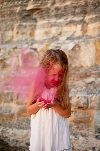 Holčička s dlaněmi foukání na Holi růžové barvy. Velký okamžik. — Stock fotografie