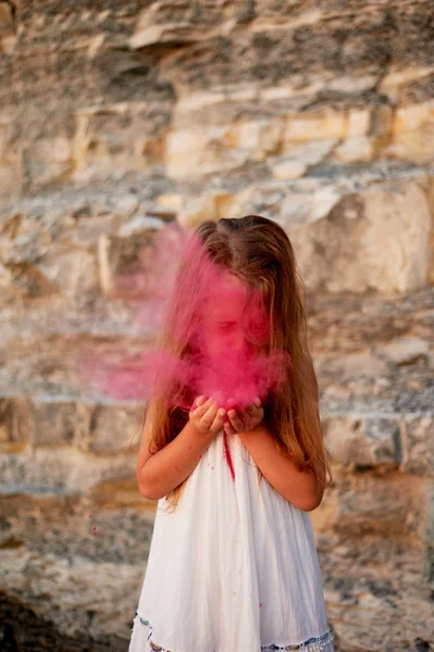 Holčička s dlaněmi foukání na Holi růžové barvy. Velký okamžik. — Stock fotografie