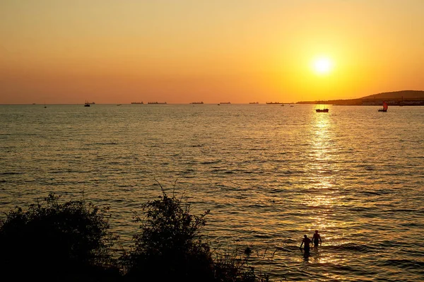 Golden sunset denizde su üzerinde yol. İnsanların yüzme, gemi siluetleri