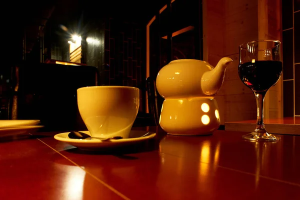 A glass of wine in a night restaurant, a teapot with a warming candle.A cozy evening in a romantic atmosphere