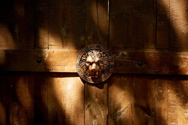 La lumière du soleil illumine les plis de l'ancienne porte en bois avec un emblème de lion métallique. La forteresse historique — Photo