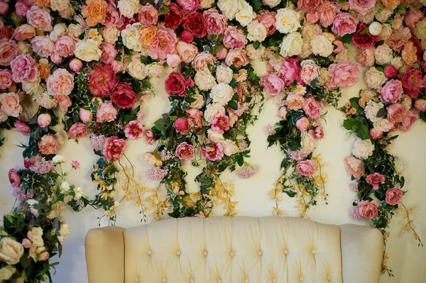 Cama velha esculpida com estofos macios contra uma parede branca decorada com flores rosadas.Lindo guirlanda. A decoração interior é romântica, zona de fotos do casamento . — Fotografia de Stock