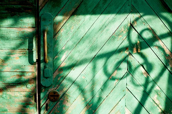 Antigua puerta verde o pared de una casa de madera en estilo rústico, con pintura pelada.La sombra de una barra de hierro forjado, dibujo en blanco y negro — Foto de Stock