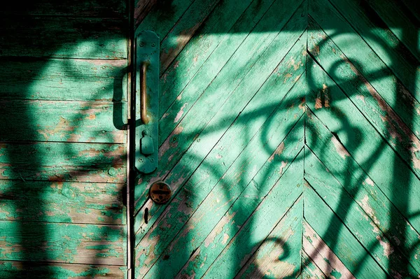 Antigua puerta verde o pared de una casa de madera en estilo rústico, con pintura pelada.La sombra de una barra de hierro forjado, dibujo en blanco y negro — Foto de Stock