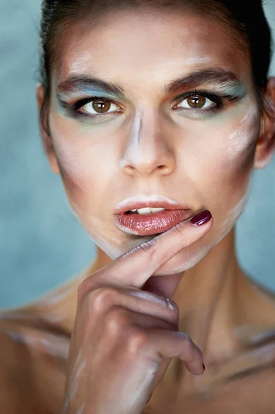 Tjej modell med kreativa makeup, penseldragen i ansiktet. Kreativ person. Finger i munnen. Ser fundersam — Stockfoto