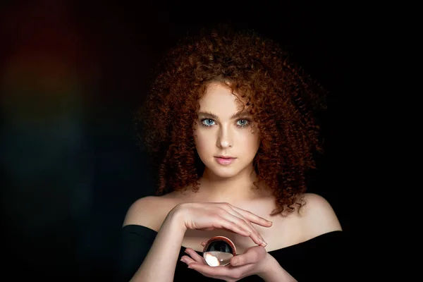 Ein Mädchen mit üppig lockigem rotem Haar. hält in seinen Händen eine Glaskugel. Geheimnis, eine Vorahnung der Zukunft. — Stockfoto