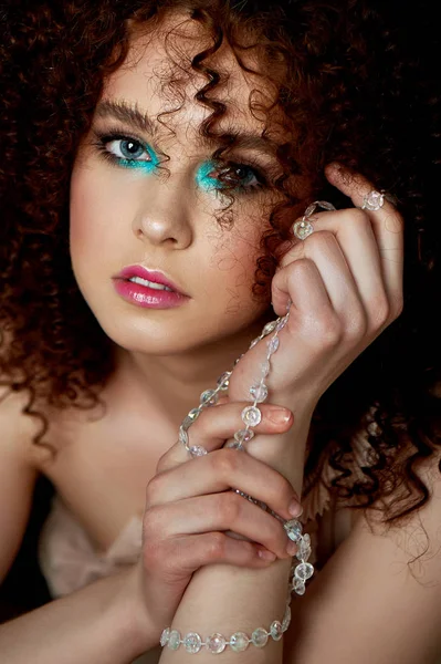 En flicka med lummiga lockigt hår. Delikat makeup med lösögonfransar i docka stil. På trådar kristall pärlor. Bijouterier — Stockfoto