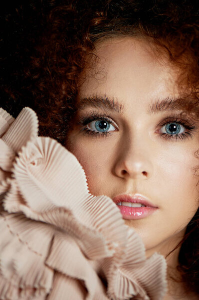 A girl with lush curly red hair. Delicate makeup with false eyelashes in doll style. Ruches cream color.