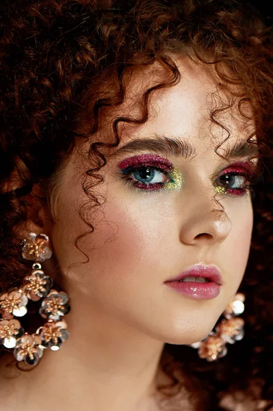 Девушка с пышными вьющимися рыжими волосами. Закрытое лицо с ярким макияжем и массивными серьгами. Пурпурные тени . — стоковое фото