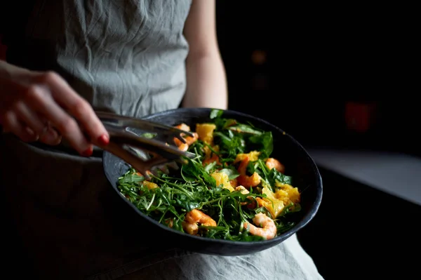 Healthy diet. Salad of arugula, tiger prawns and oranges. Light dish with seafood. Diet menu. Hands interfere salad — Stock Photo, Image