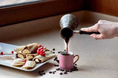 Çikolata yayıldı ve muz krep tatlı sıcak. Kuş üzümü ile dekore edilmiştir. Şekerli tatlı. Sırada bir fincan kahve var. Turki el dökerek kahve