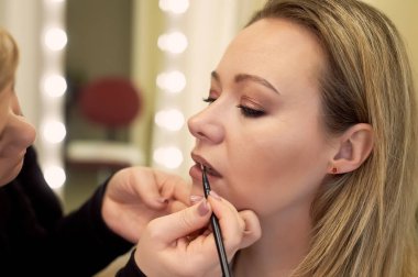 Makyaj sanatçısı müşterilerin dudaklarının kontur yapar. Stil seçimi. Güzellik sektöründe çalışmak.