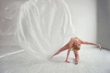 Jimnastikçi beyaz bir duvar ve zemin üzerinde şeffaf bir film ile dans. Zarafet ve sağlıklı yaşam tarzı.