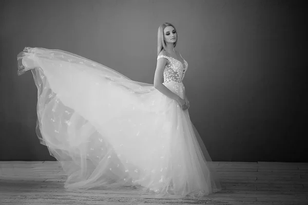 Belo vestido de renda, perfeitamente sentado na figura.Uma noiva bonita fica em uma sala de estilo loft, joga-se uma saia de um vestido de noiva exuberante . — Fotografia de Stock
