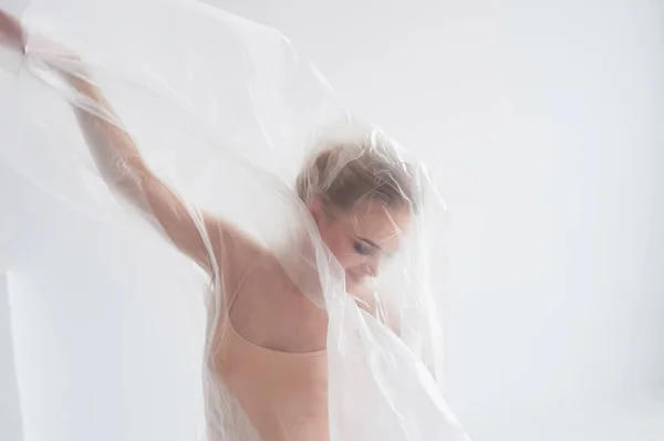 Turnerin tanzt mit transparenter Folie auf weißer Wand und Boden.Anmut und gesunder Lebensstil. — Stockfoto
