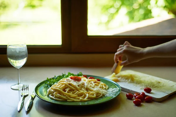 Pasta Carbonara z tartą parmezanem i pomidorami wiśniowym, ozdobiona arugula. Włoski obiad. Ręka womans stawia kawałek sera. — Zdjęcie stockowe