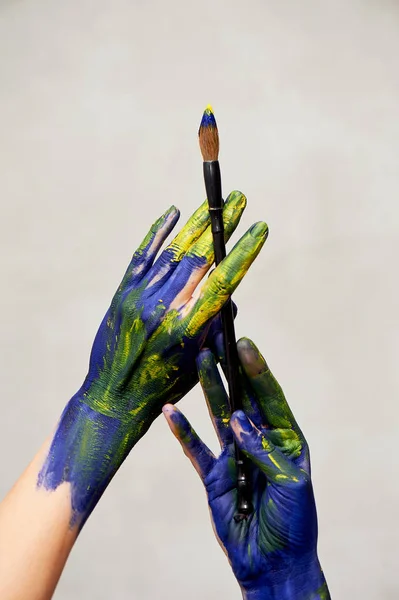 Mani graziose dell'artista con un pennello. Mani in vernice blu e gialla.Creatore, creatività . — Foto Stock