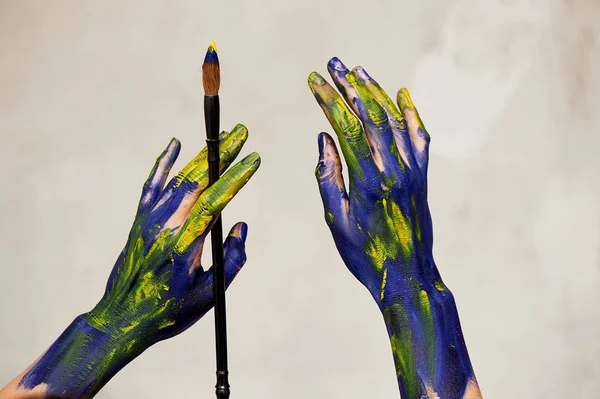 Mani graziose dell'artista con un pennello. Mani in vernice blu e gialla.Creatore, creatività . — Foto Stock