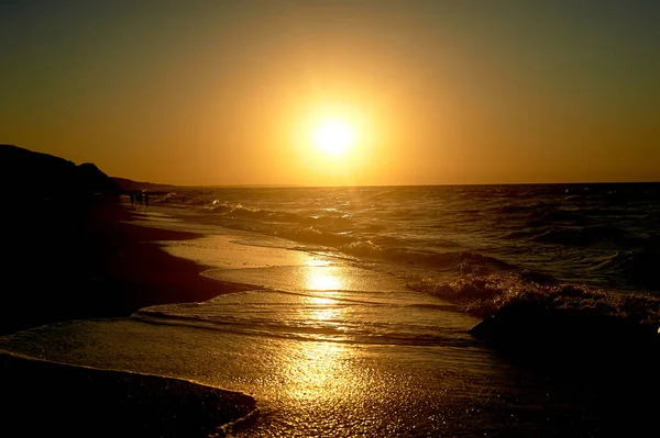 Meer goldenen Sonnenuntergang. Wellen laufen auf dem sandigen Ufer. Silhouetten von Menschen, die am Ufer entlang gehen. — Stockfoto