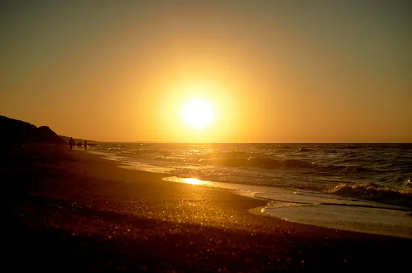 Meer goldenen Sonnenuntergang. Wellen laufen auf dem sandigen Ufer. Silhouetten von Menschen, die am Ufer entlang gehen. — Stockfoto