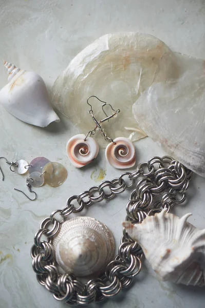 灰色の大理石の背景に海のコレクション。貝殻とマザーオブパールのイヤリング。夏のジュエリー。メタルチェーン、マザーオブパールシェル — ストック写真