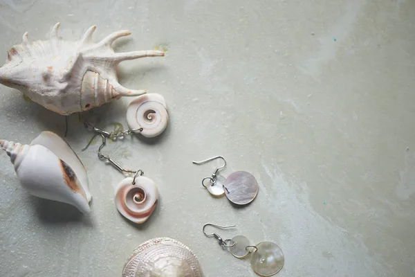 Sea collection on grey marble background. Seashell and mother-of-pearl earrings. Summer jewelry.
