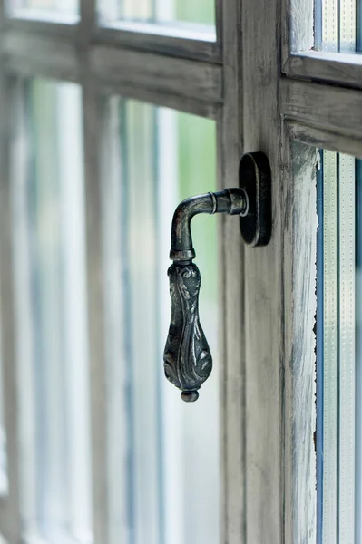 Forged handle on a light-colored wooden window.Classical interior